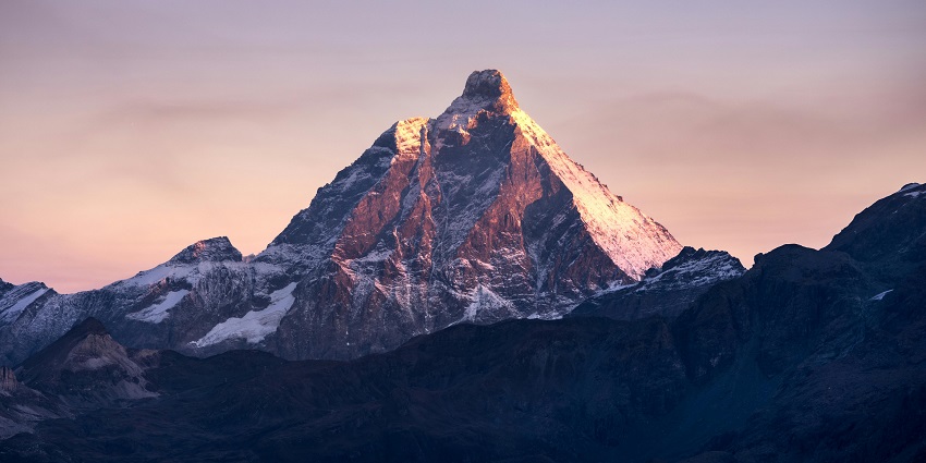 Snow-capped mountain peak glowing in the soft light of sunrise against a pastel sky
