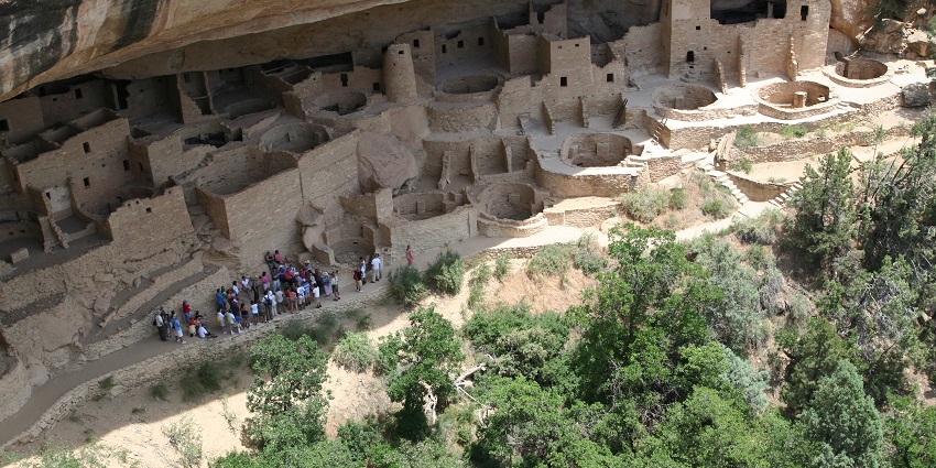 Old Ancestral Puebloan cliff dwellings at Mesa Verde with tourists visiting the site.