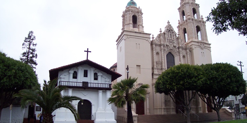 Two churches side by side, one small and simple, the other tall with ornate towers.