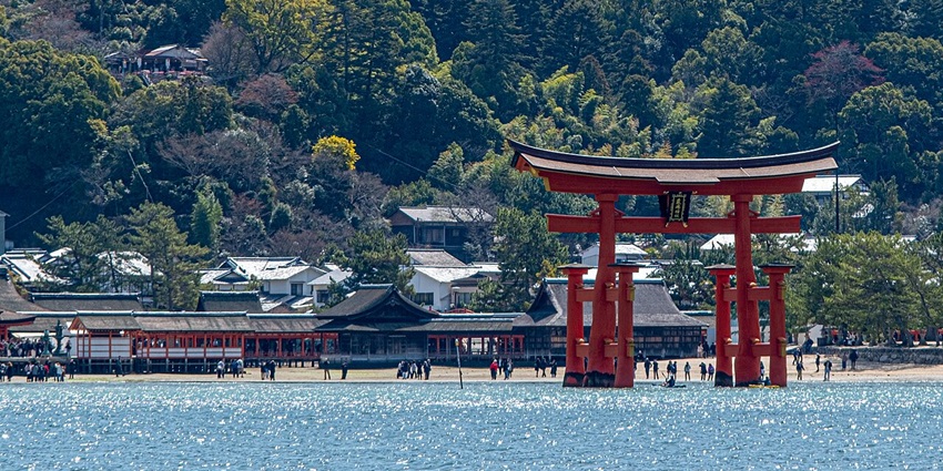 The famous red torii gate of Itsukushima Shrine stands in the sea with forested hills behind.