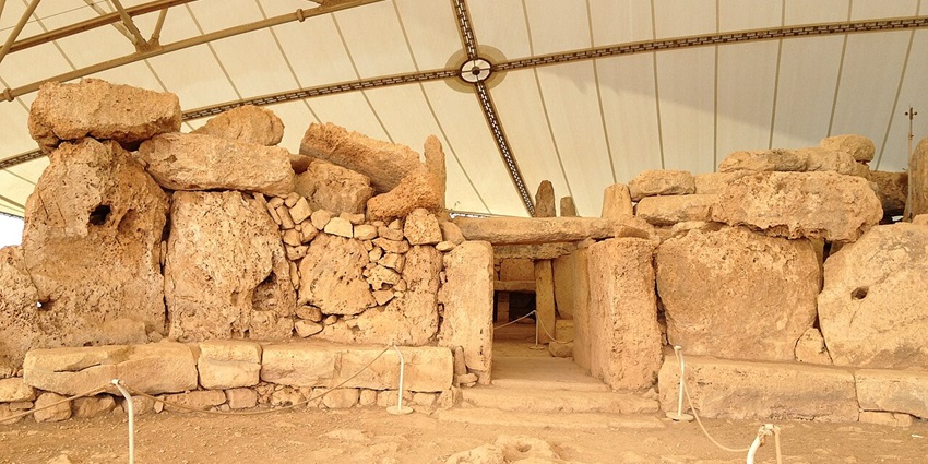 Mnajdra temples with big rock structures, brown grass bushes and the sea at a distance
