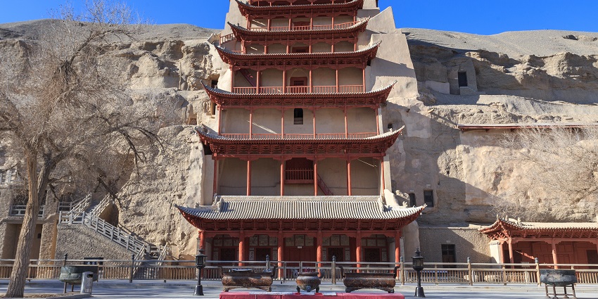 Exterior of Mogao caves in Dunhuang with classic Chinese architecture and dried-out trees