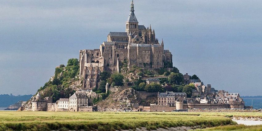 The Mont Saint-Michel abbey is atop a rocky island surrounded by grassy marshes and tidal waters.