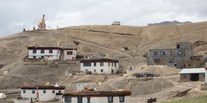 Buddha statue on a medium-sized rocky hill with a few houses on the rocks with a clear sky.