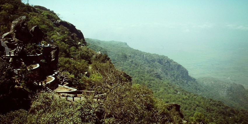 Honeymoon point at Mount Abu with small green bushes, distant green hills and buildings.