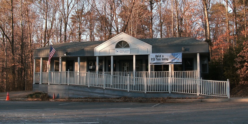 Small United States Post Office building with ramp and banner promoting P.O. box rental.