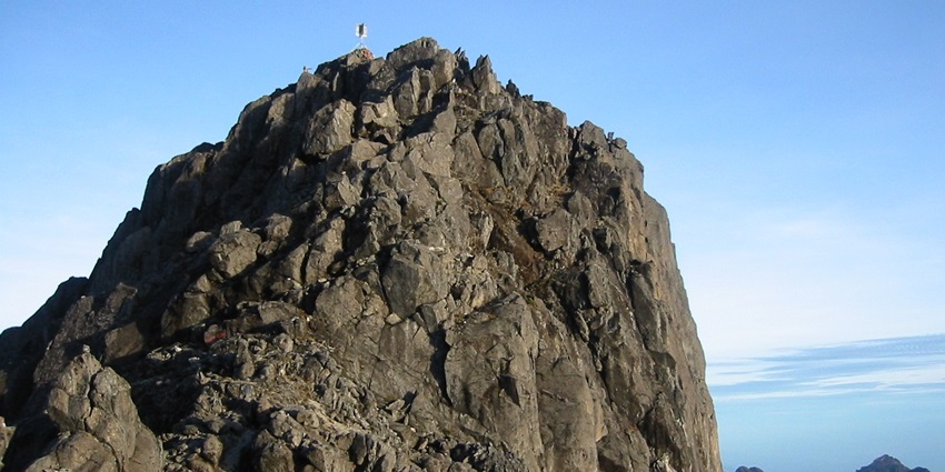 Rocky Peak of Mount Wilhelm with hills at a distance under a cloudy blue sky, one of the historical places in Papua New Guinea.