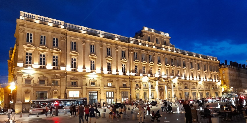 Musée des Beaux-Arts de Lyon in the evening with an illuminated facade, people and vehicles