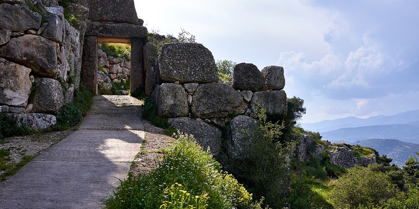 Ruins of an ancient stone structure at Mycenae, overlooking a lush valley and mountains.