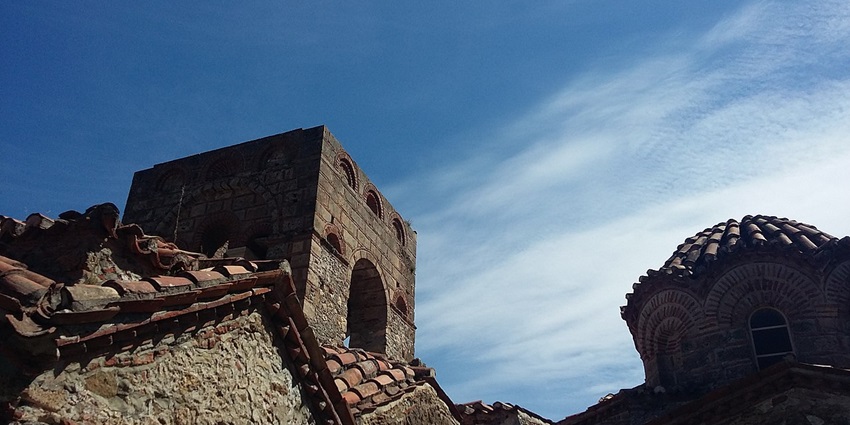 Stone tower and domed Byzantine church with tiled roofs under a bright blue sky.