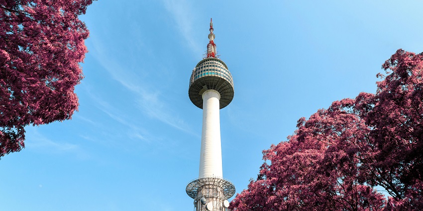 Scenic view of N Seoul Tower against a cloudy sky, surrounded by trees, showcasing a popular landmark in Seoul, South Korea.