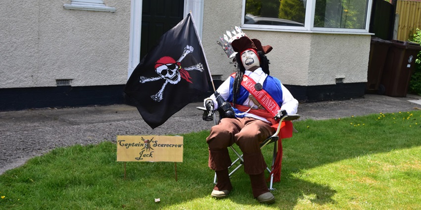 Scarecrow village with a doll on the chair, black skull flag and wooden signage board