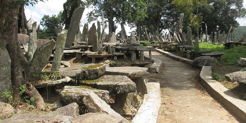 Nartiang monoliths with unique rock structures, tall green trees, grass and walking path.
