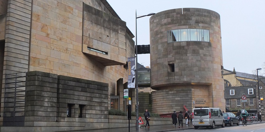 Modern stone building of the National Museum of Scotland with people walking on a street.