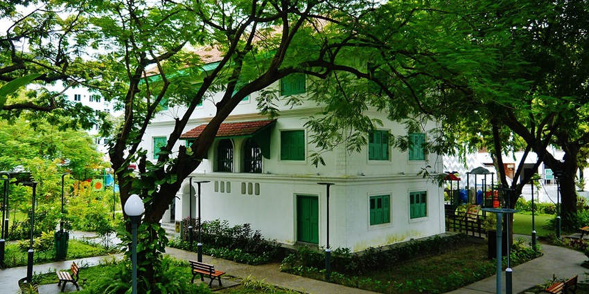 Sultan Park with pathways and benches and a white-green building surrounded by greenery