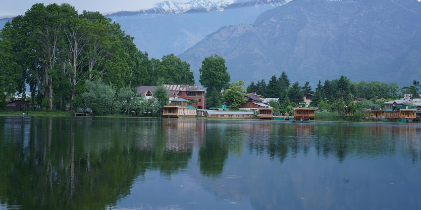 Serene lake with clear waters, surrounded by houseboats, gardens, and Himalayan views