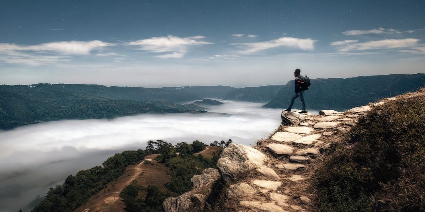 Nongjrong viewpoint in midnight with a man standing near cliff, clouds and stone trail.