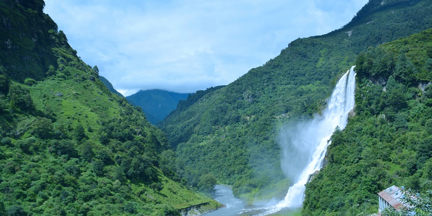 Nuranang waterfall in Tawang, with water flowing into a small river and green mountains