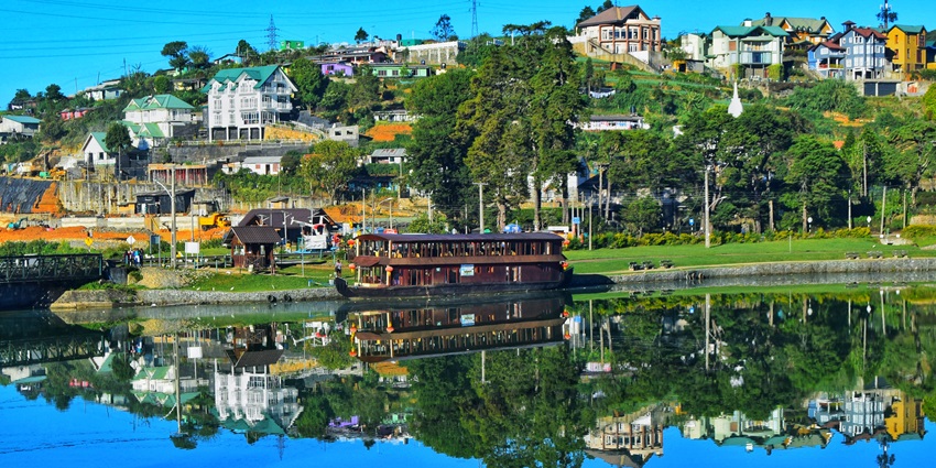 A scenic view of Gregory Lake with crystal clear water and scattered houses in Nuwara Eliya.