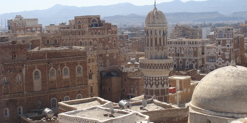 Ancient cityscape with densely packed mud-brick buildings and tall tower structures.