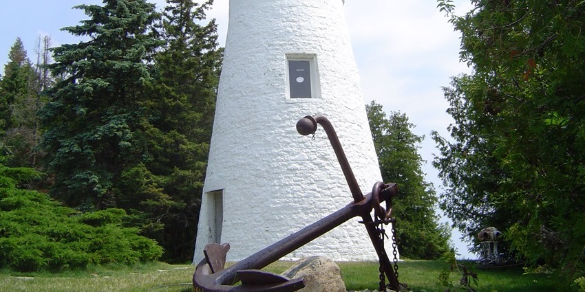 Old Presque Isle lighthouse in Michigan with a tall white building, a sitting bench, and green trees