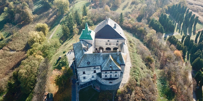 Aerial view of a historic stone castle surrounded by trees and green hillside, one of iconic historical places in Ukraine.