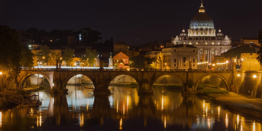 A heavenly night view of a beautiful church overlooking a bridge running across a water body.