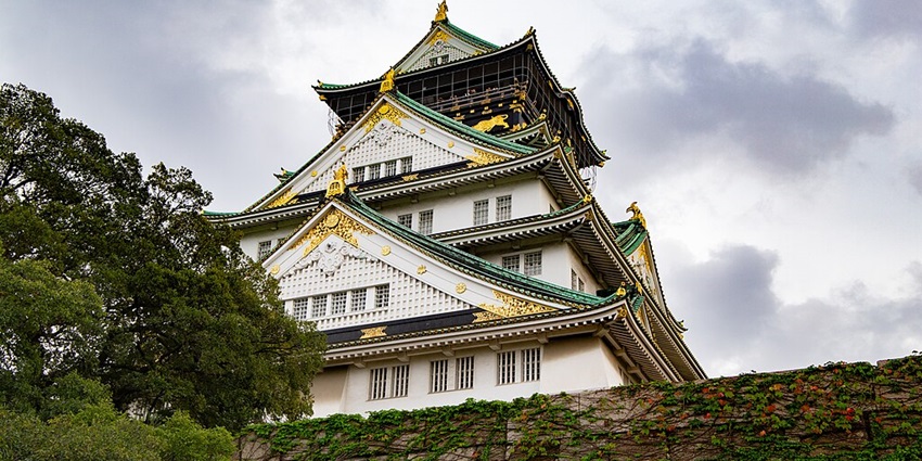 Majestic white castle with green and gold roof details, set above a stone wall and trees.