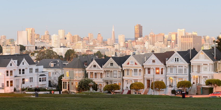 Colourful Victorian houses with a grassy park in front and a city skyline, San Francisco