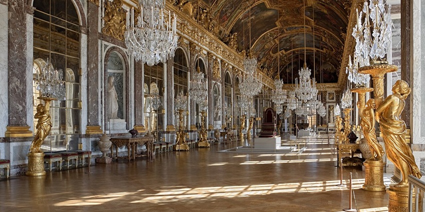 The Hall of Mirrors at Versailles with chandeliers, gold decor, and an arched ceiling.