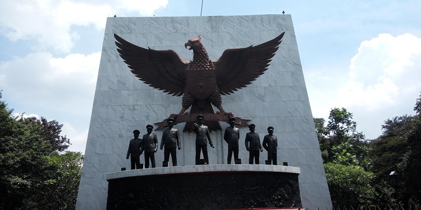 A marble structure displays a bronze Garuda bird emblem above life-sized statues of seven uniformed military figures.