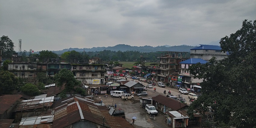Pasighat town from above with multiple vehicles parked, old buildings and mountains