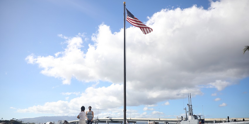 Tourists at Pearl Harbor memorial site with the American flag and historic submarine in sight.