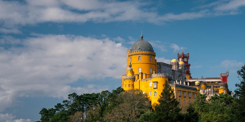 Colorful towers and domes of Pena Palace atop a forested hill in Sintra, is one of the most beautiful historical places in Portugal