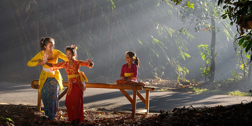 Two girls dancing in traditional dresses and one sitting with the bamboo forest.
