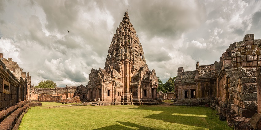 Ancient stone temple ruins of Phanom Rung, surrounded by trees and a cloudy sky, displaying Khmer architecture in Thailand.