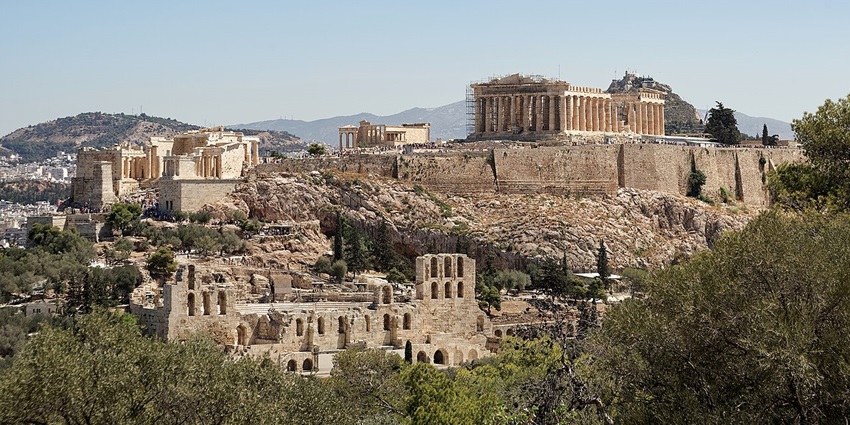 Ancient hilltop ruins with classical columns and stone structures surrounded by greenery.