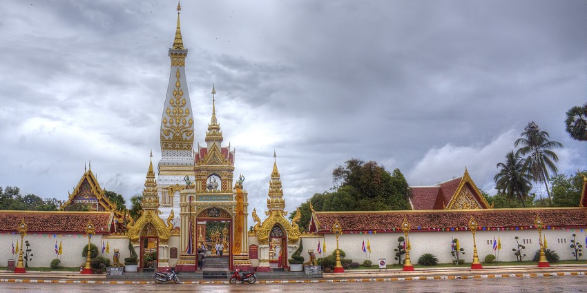 Golden Buddhist temple courtyard at dusk with statues, lamps, and a tall central stupa.