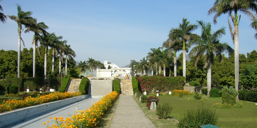 A scenic view of Pinjore Gardens in Chandigarh, featuring terraced lawns, fountains, Mughal architecture, and dense greenery under sunlight.