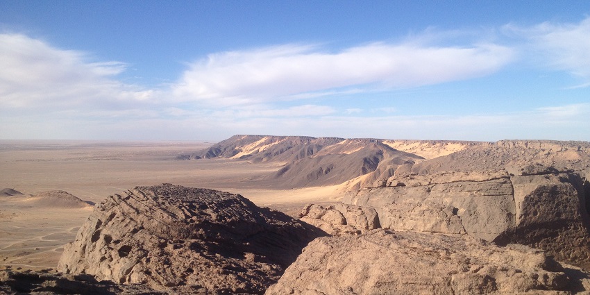 Plateau of Djado with sandy plains surrounded by small rocky hills under a blue cloudy sky