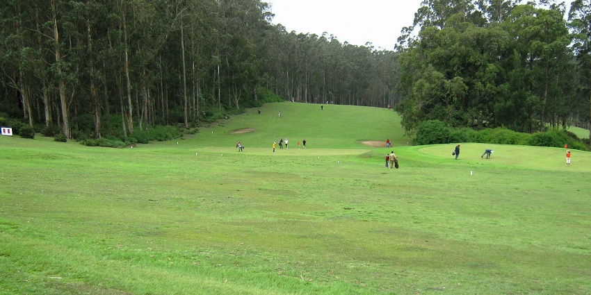 Golf course in the early morning in Shillong with yellow sunrays hitting the tall green trees, one of the best places to visit in Shillong in October.