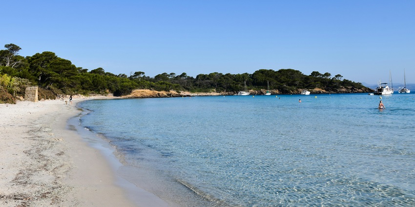 Yachts anchored near Porquerolles Island's sandy beach with clear blue sea and sky .