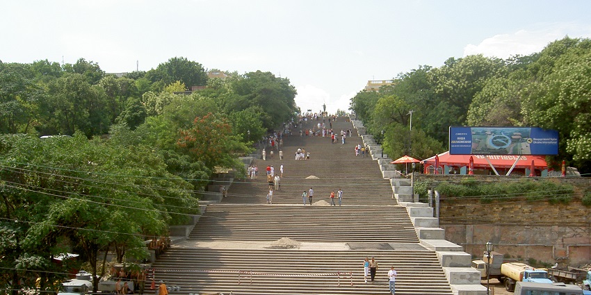 View of Potemkin Stairs in Odesa, leading up from the harbour, lined with trees and visitors.
