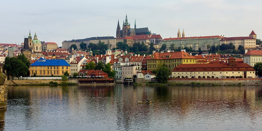 Image of the Prague Castle with city buildings and a river in the foreground.