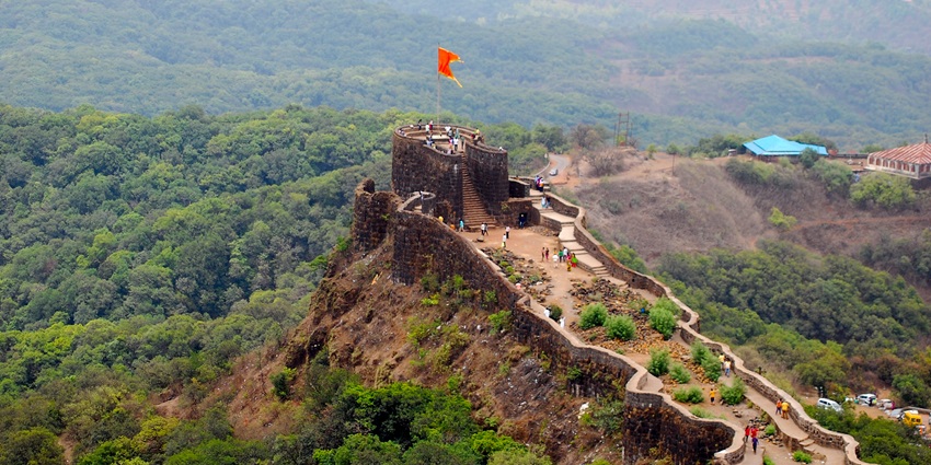 A fort situated on a hilltop surrounded by dense greenery and showing a lively atmosphere.