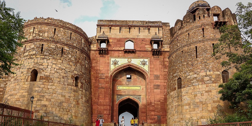 Entrance of the Purana Qila complex with ancient stone walls and green lawns around.