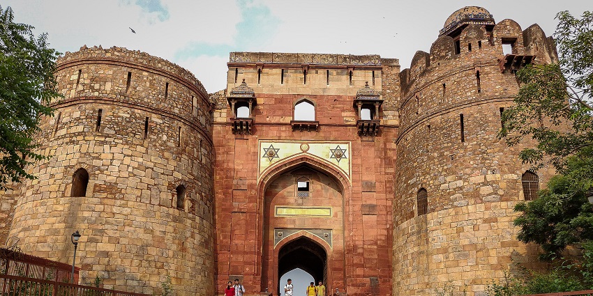 Ancient stone walls and gateways of Purana Qila complex with green lawns around.