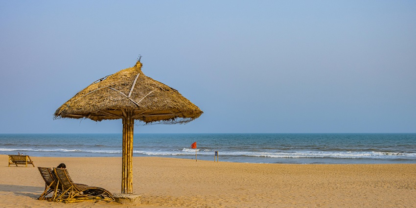 Puri beach in Odisha with sandy shores, calm waters and wooden lounge chairs.
