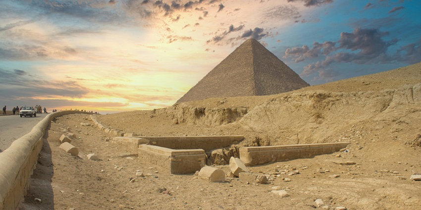 The Great Pyramid of Giza at sunset with a desert path and scattered ancient ruins nearby.