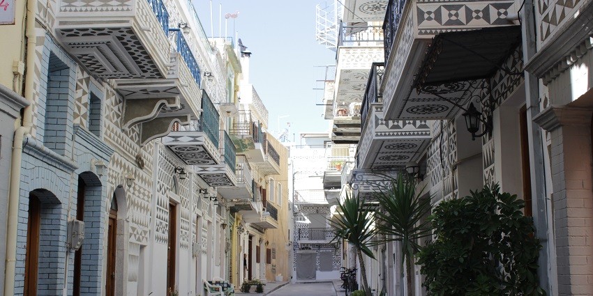Street of Pyrgi village in Chios with Greek houses on both sides and lamps on walls.